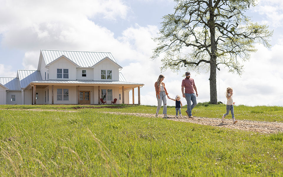 Family of four walking down the driveway with their rural family home in the background.