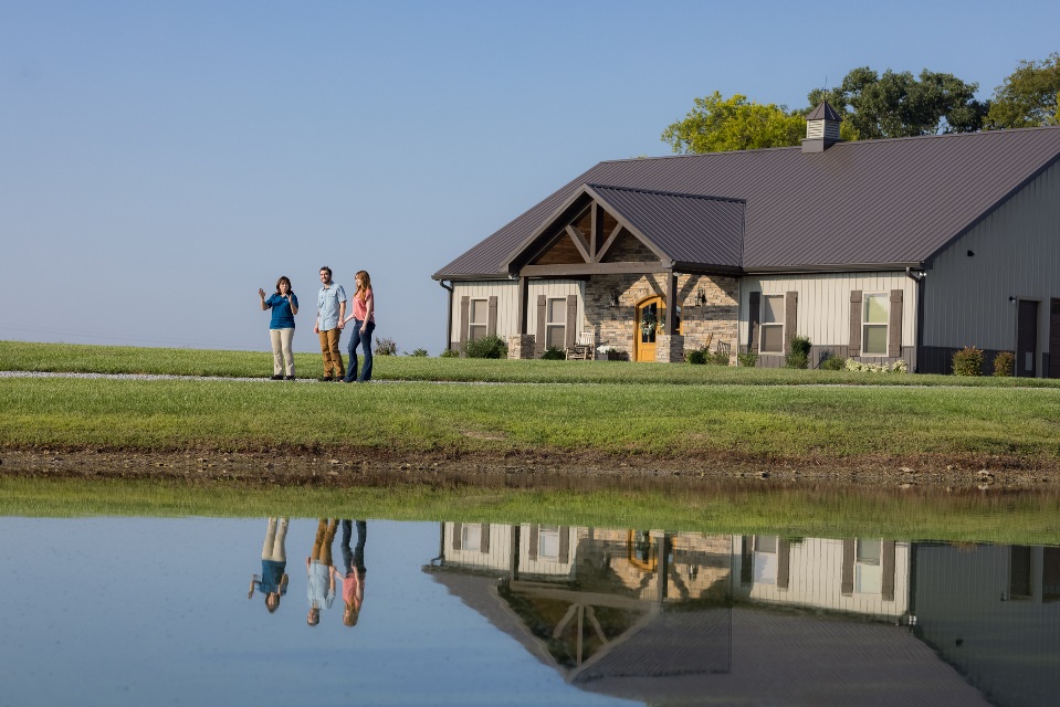 Man and woman talking with loan officer by a pond with a home in the background