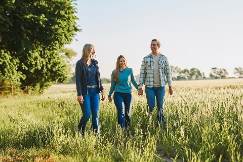 A young couple walks through a field of tall grass with a Rural 1st loan officer