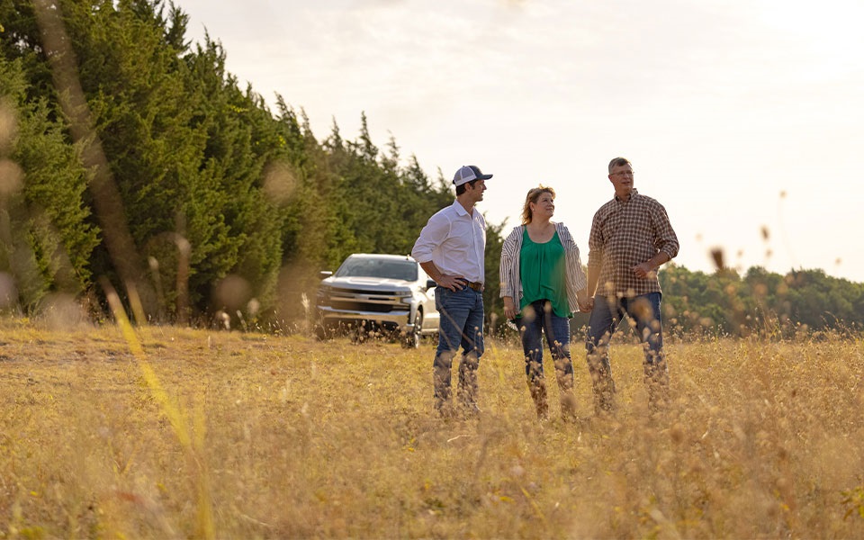 A Rural 1st loan officer with a couple in a rural field that was bought with a lot loan.