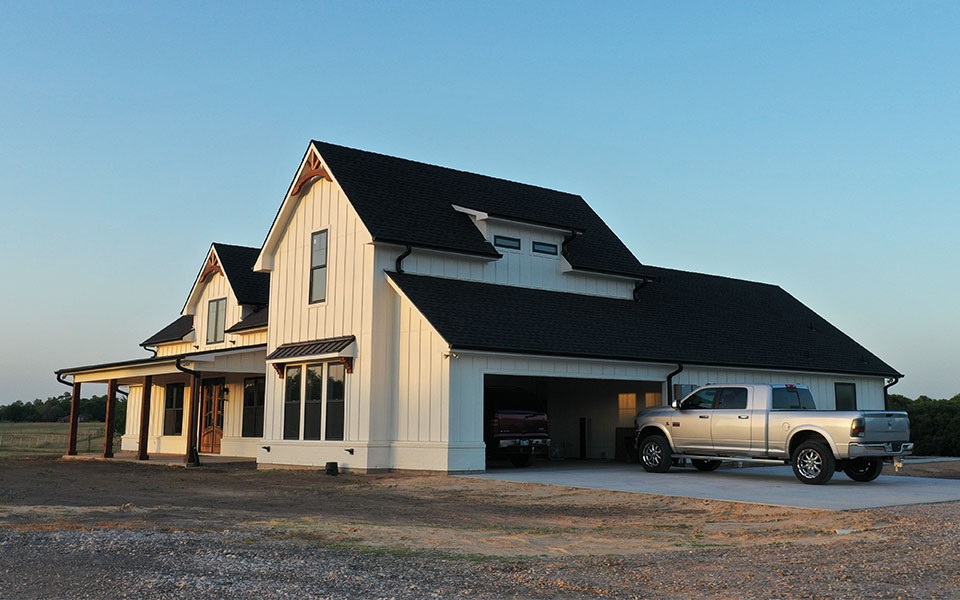 A pickup truck parked in the driveway of a newly constructed rural home.