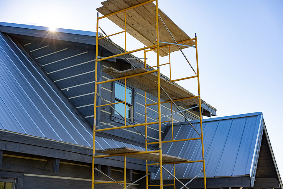 Metal construction scaffolding rises high in front of a modern log home.