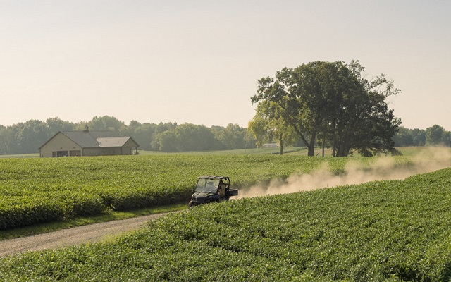 A utility vehicle driving down a rural road between farm fields.