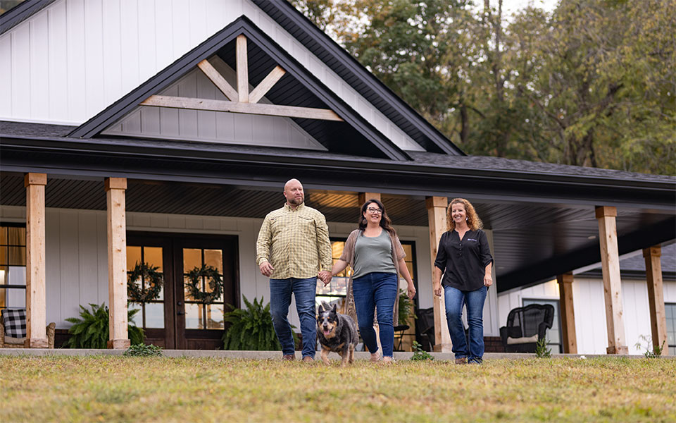 A couple walking and talking with a Rural 1st home loan officer in front of their rural dream home in the country.